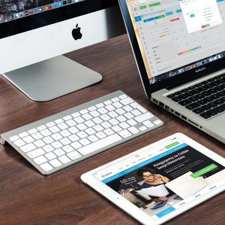 A sleek office desk setup featuring Apple devices: iMac, MacBook, and iPad.